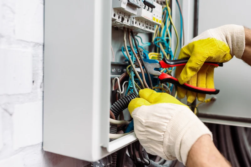 Elektryk w rękawicach ochronnych układa przewody w otwartej rozdzielnicy elektrycznej