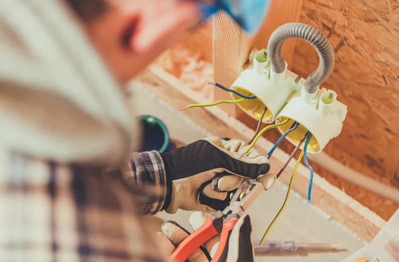 Elektryk łączy przewody w puszce instalacyjnej podczas modernizacji instalacji elektrycznej