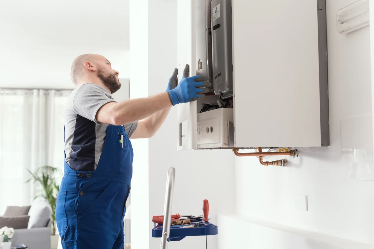 Instalator otwiera obudowę wiszącego kotła gazowego w mieszkaniu — wymiana i montaż kotłów